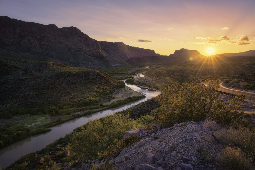 A tranquil scene with a flowing river drenched in the warm colors of sunset.